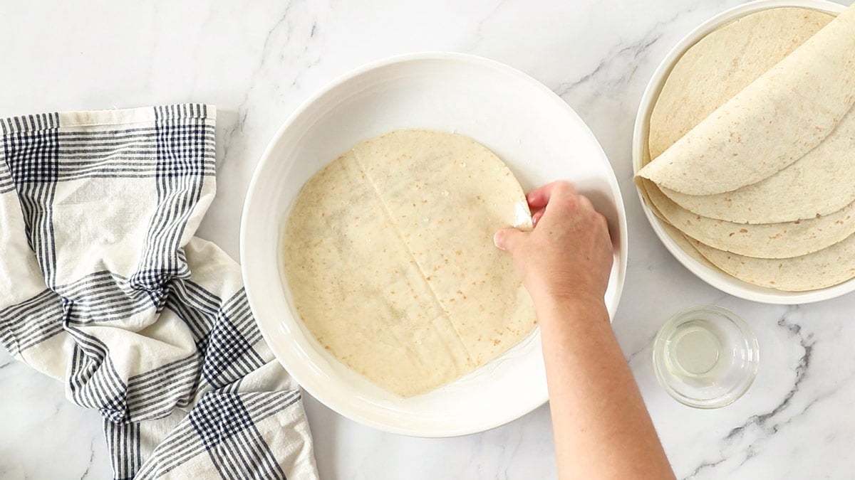 a hand dipping a tortilla into a white bowl.