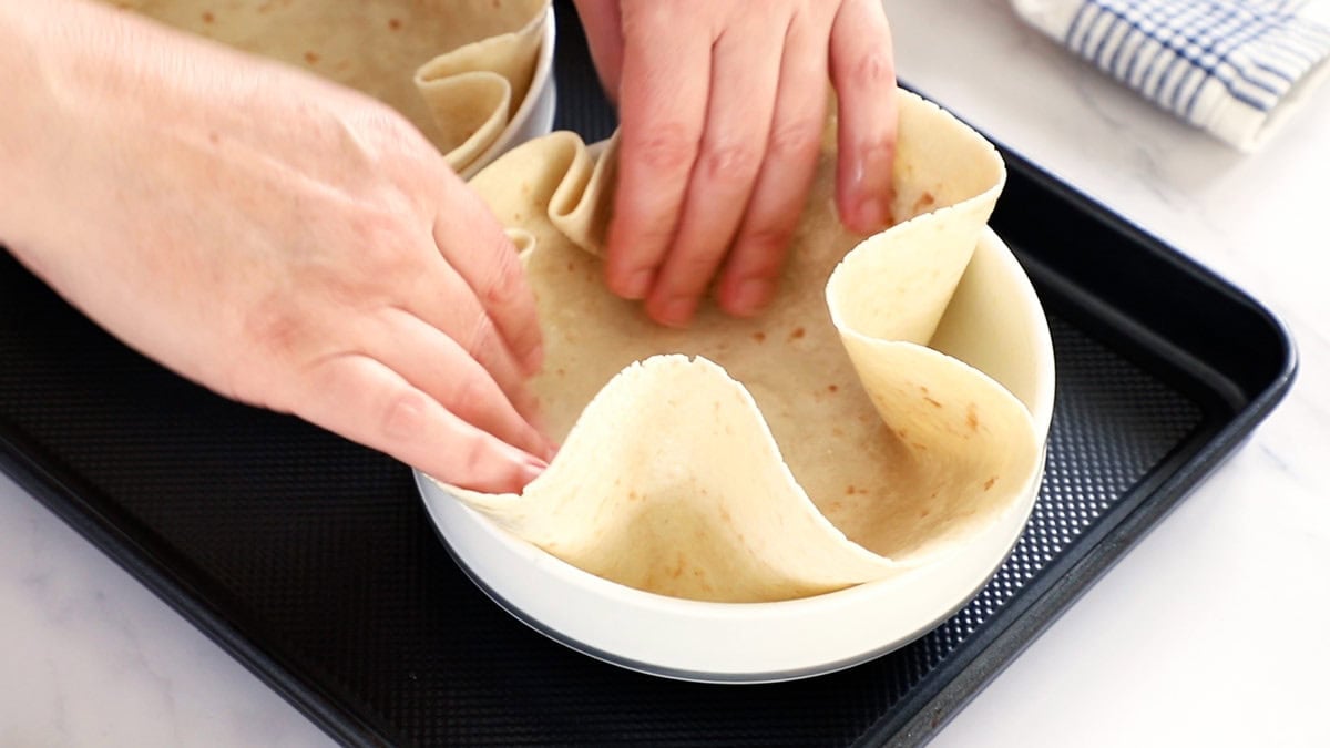 a hand forming a tortilla in a white bowl.