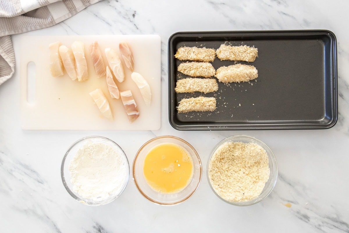 breaded pieces of mahi mahi with bowls of flour, eggs, and panko breadcrumbs.