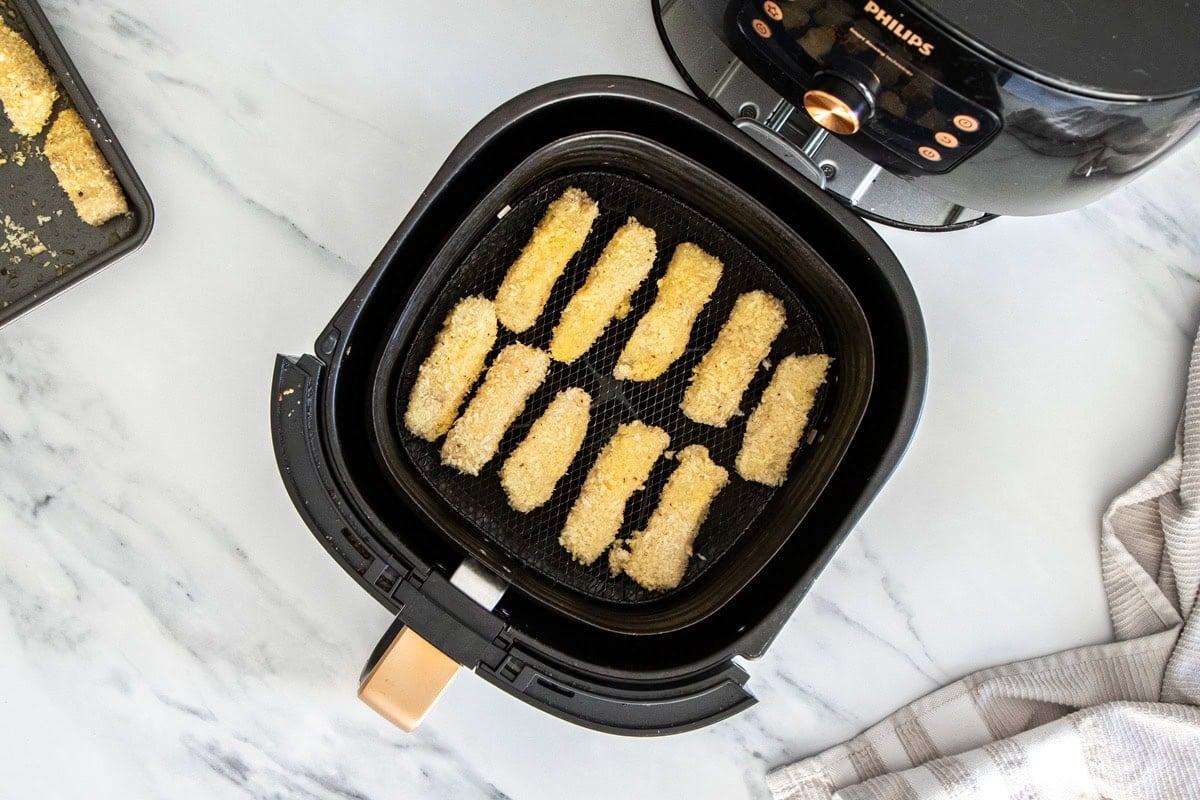 slices of crispy fish in an air fryer basket.