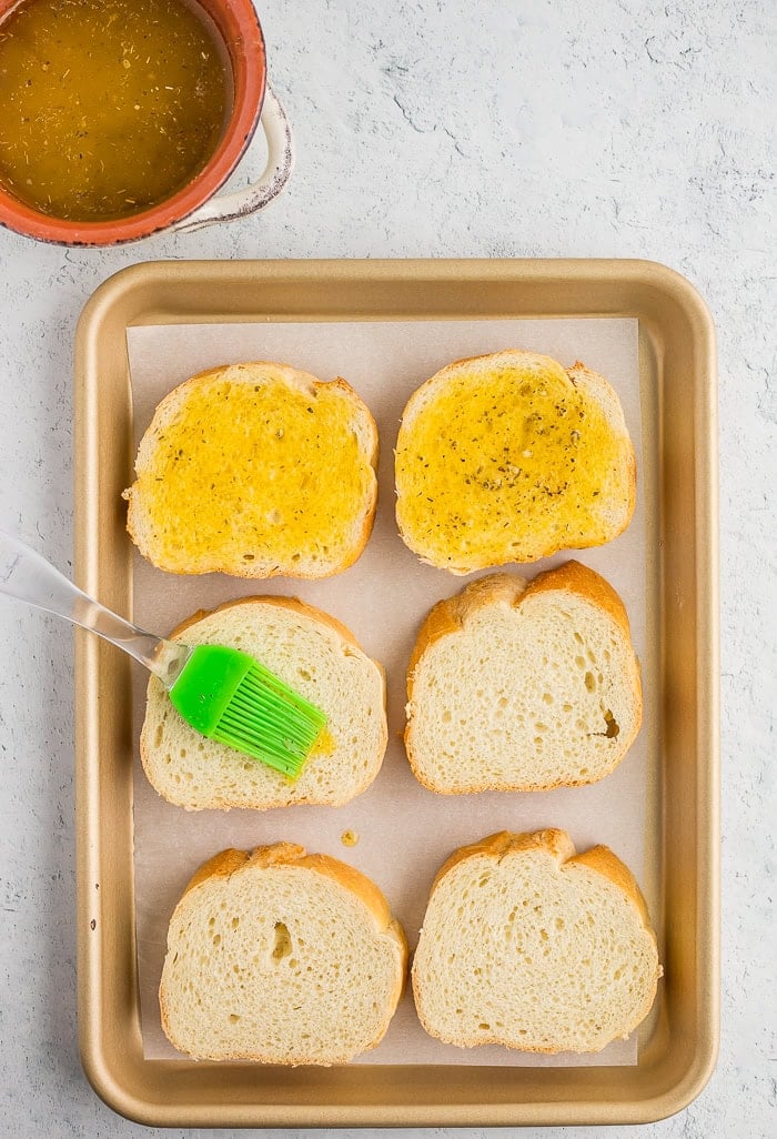 slices on bread on a baking sheet with a pastry brush and garlic butter sauce.