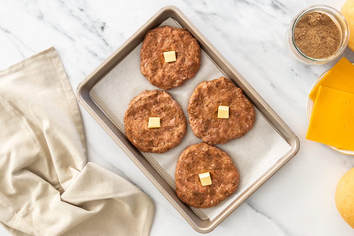 burger patties with a pat of butter on a baking sheet.