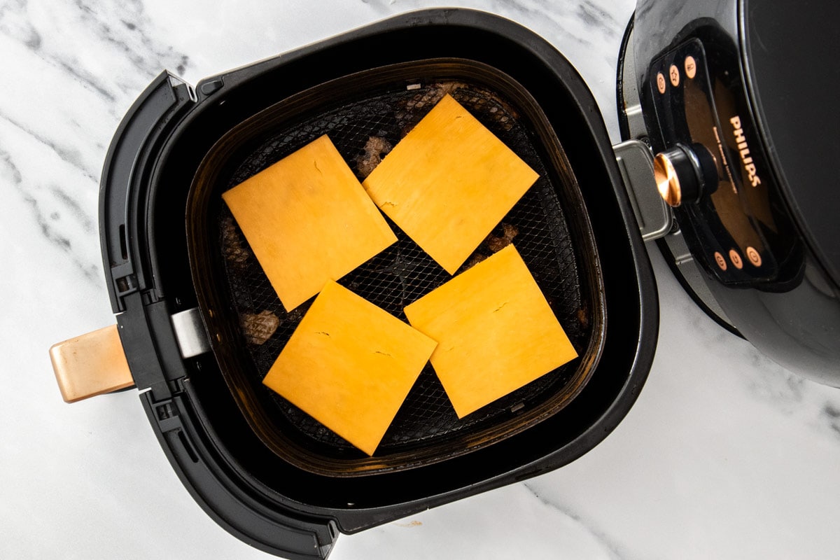 cheese on burger patties in an air fryer basket.