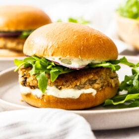 a side profile of a juicy salmon burger topped with tartar sauce, arugula, and purple onion.