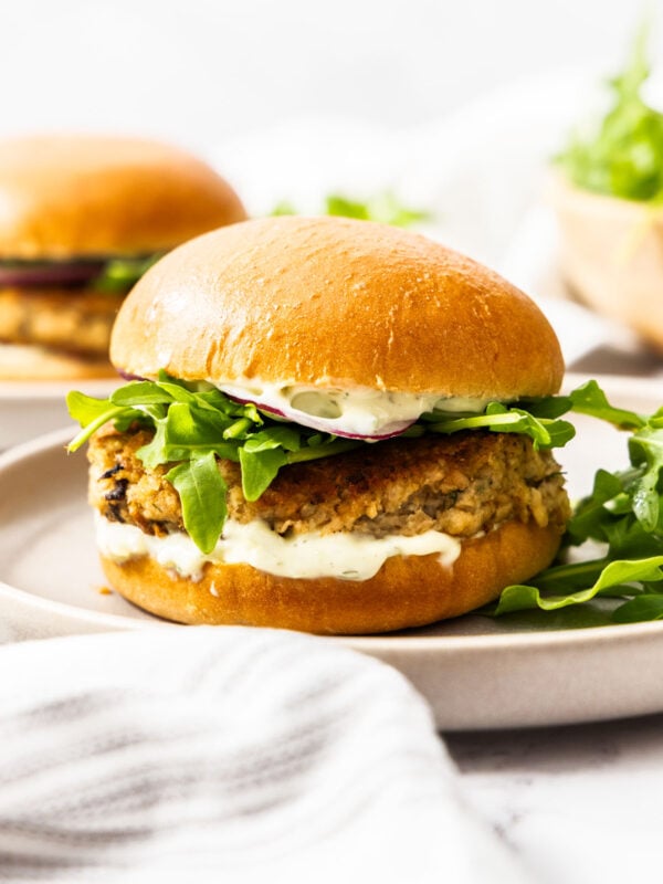 a side profile of a juicy salmon burger topped with tartar sauce, arugula, and purple onion.
