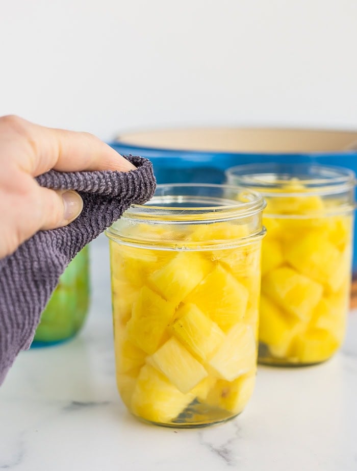 a hand with a rag cleaning the rim of a canning jar.