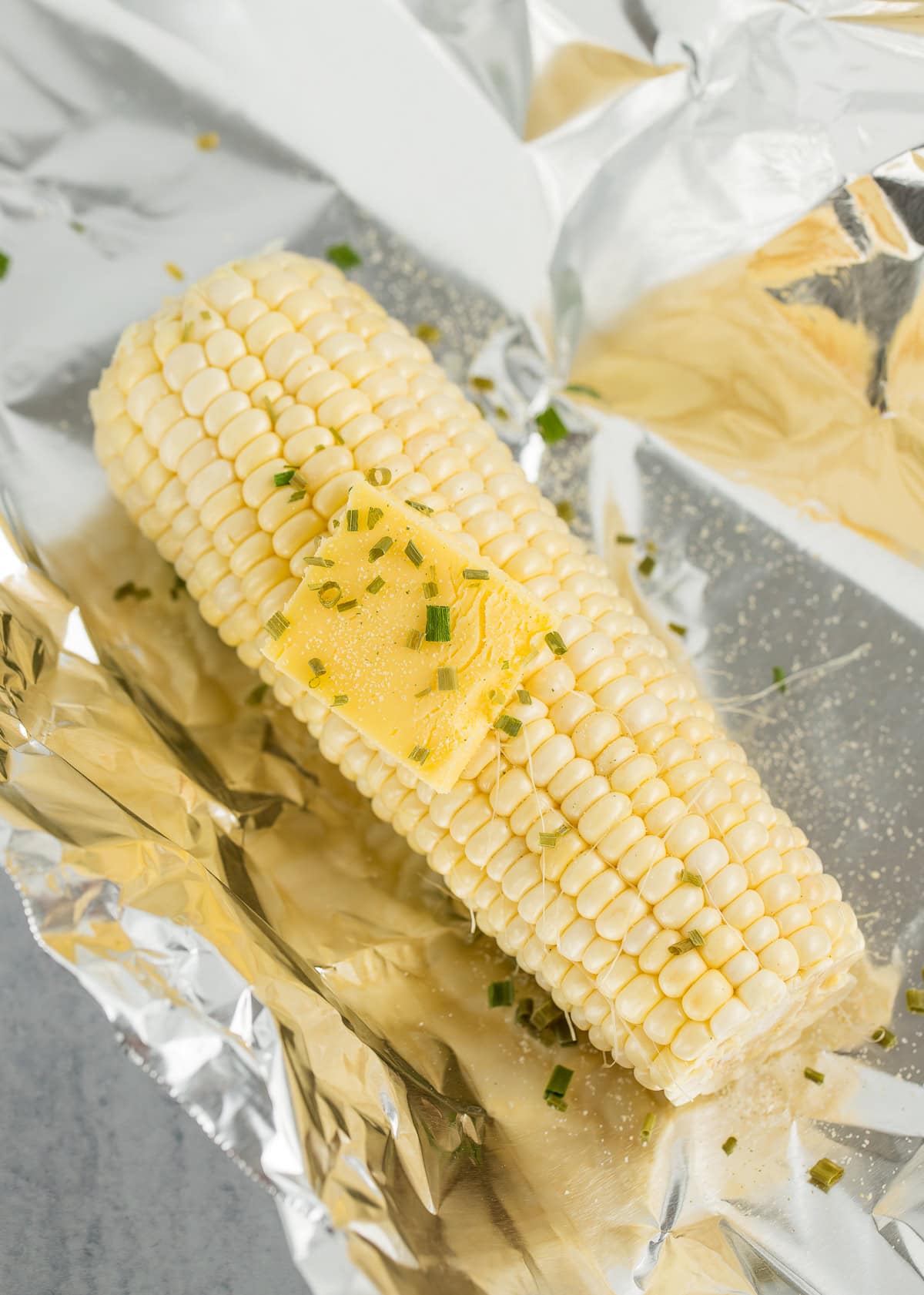 an ear of corn with a pat of butter and chives on a piece of foil.