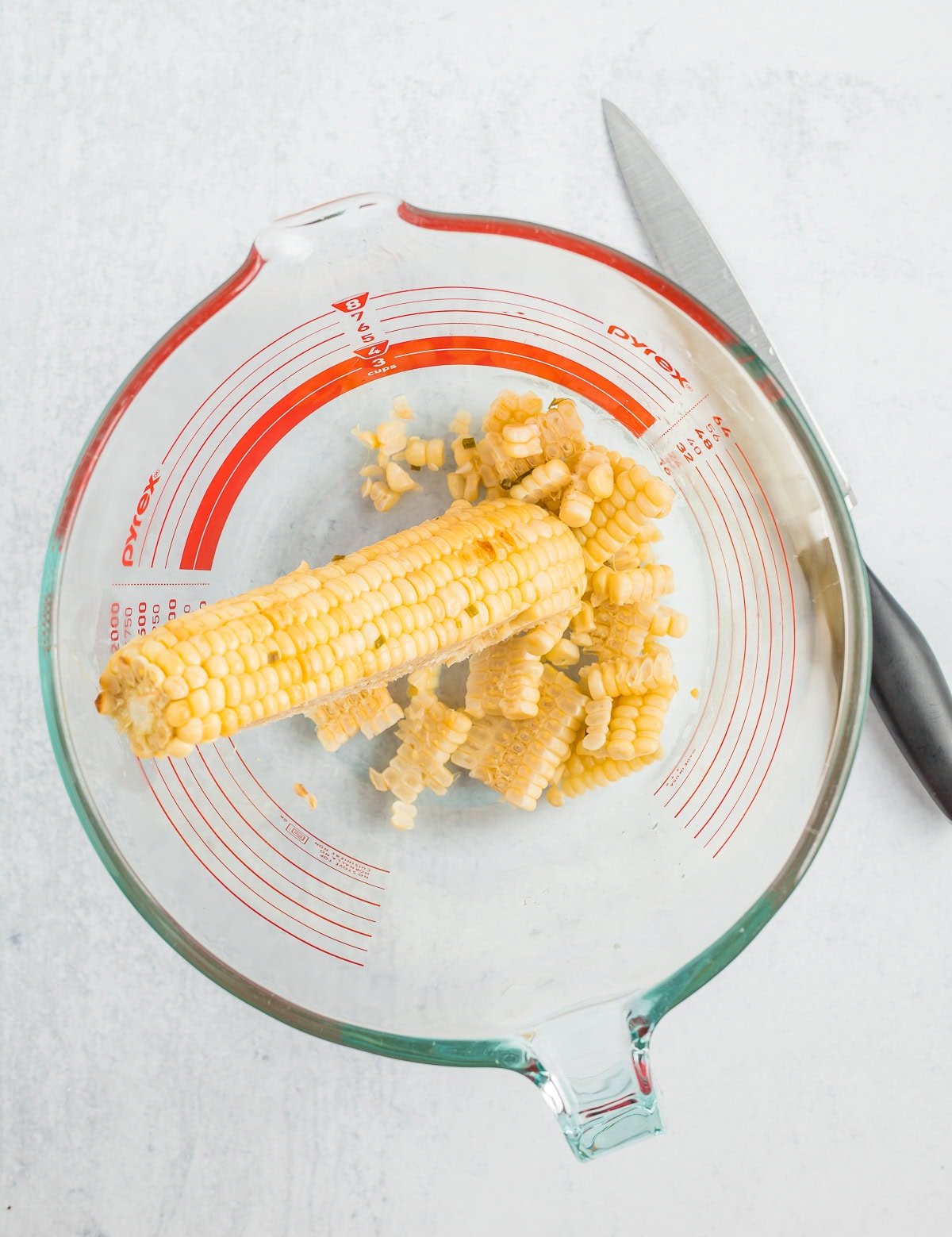 an ear of corn in a glass bowl with a knife.