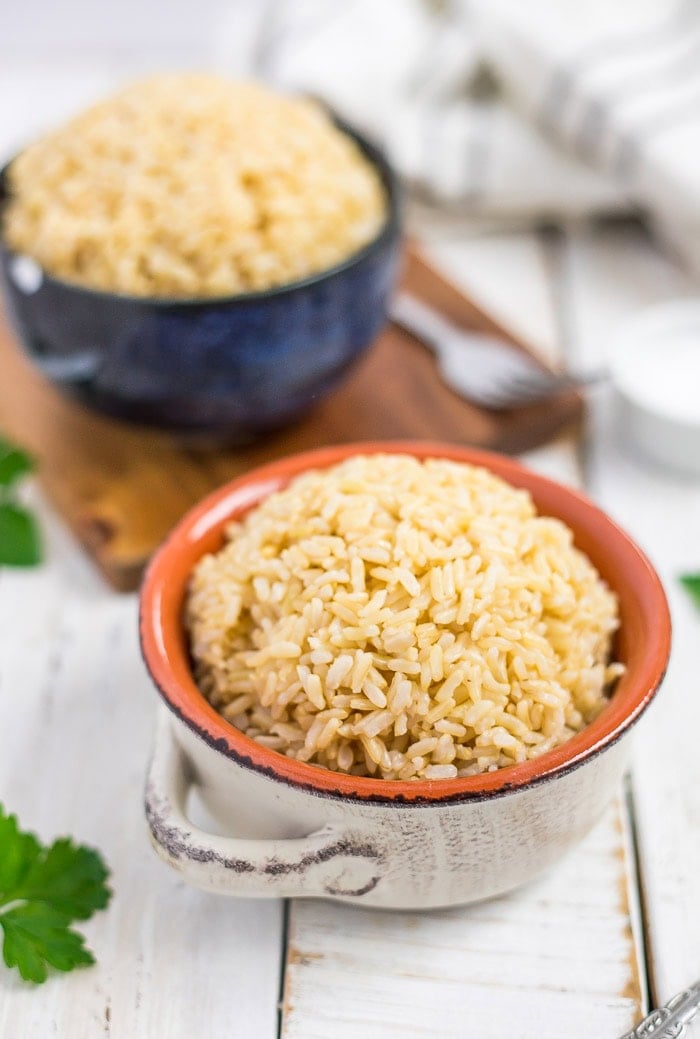 two bowls of Instant Pot brown jasmine rice on a white wooden board with fresh parsley.