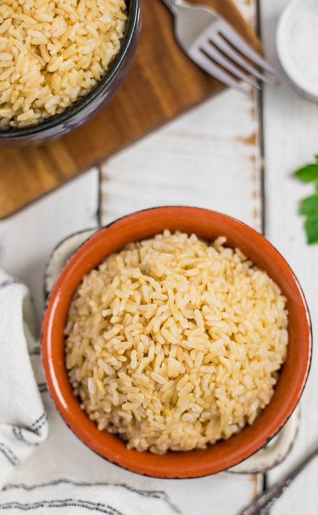 an orange bowl with cooked brown jasmine rice on a white board.