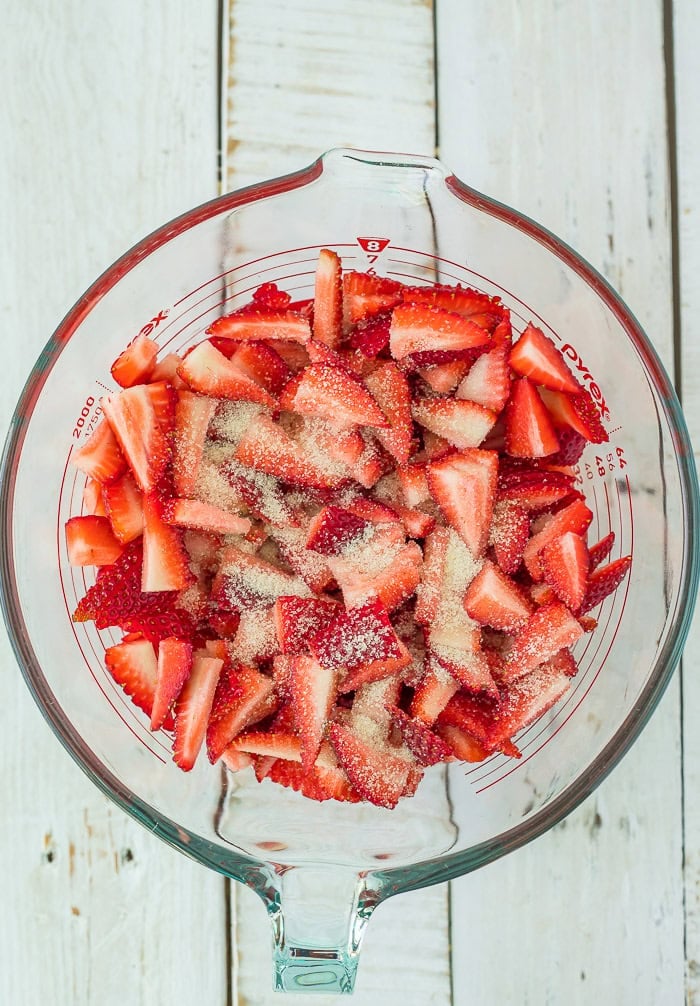 Sliced berries topped with sugar in a glass bowl.