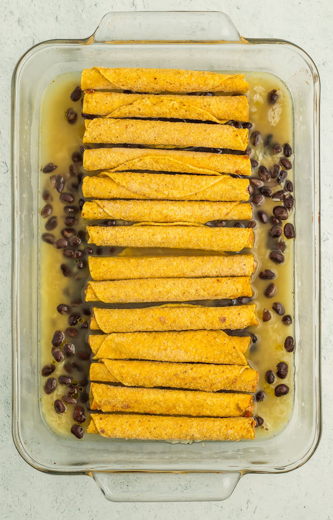 a casserole dish with beans and rolled tacos.