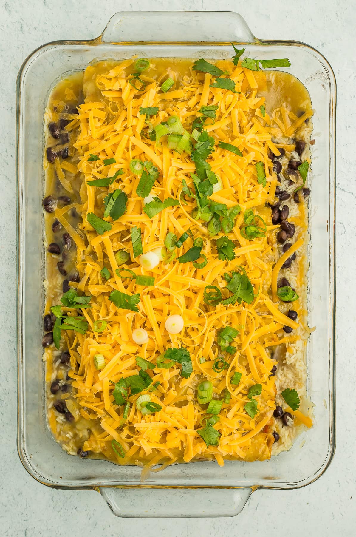 a casserole dish with taquitos and beans topped with cheese, cilantro, and green onions.