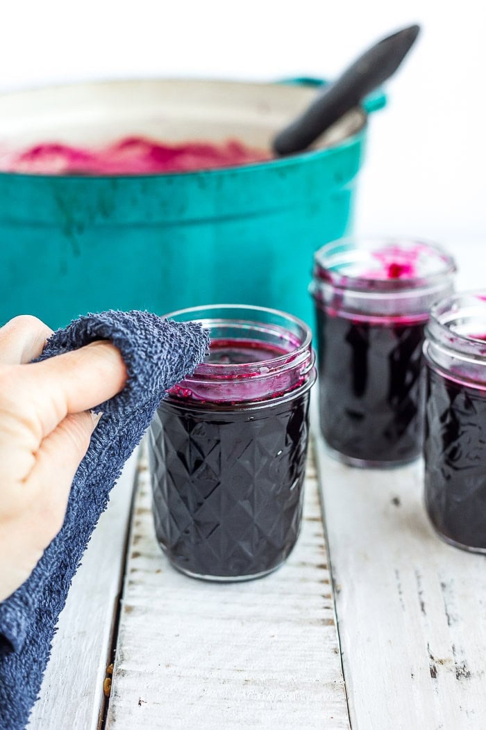 a hand with a blue rag cleaning the rim of a mason jar.