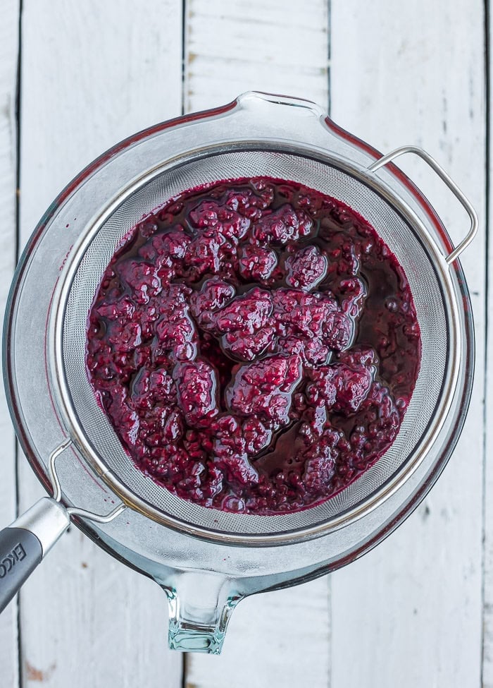 berry sauce in a sieve over a glass bowl.