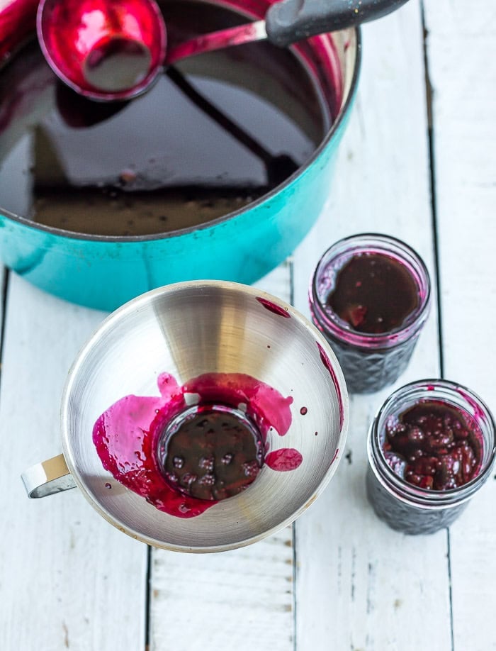 berry sauce in a funnel in canning jars.