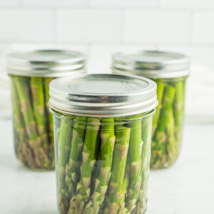 jars of canned asparagus sitting in front of a tiled wall.