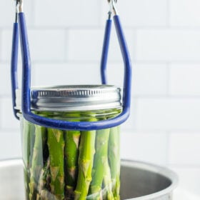 tongs with a mason jar being lowered into a stockpot.