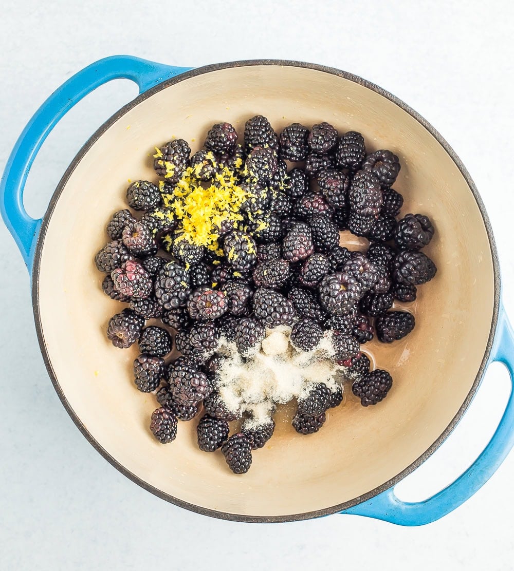 a blue dutch oven with blackberries, sugar, and lemon zest.