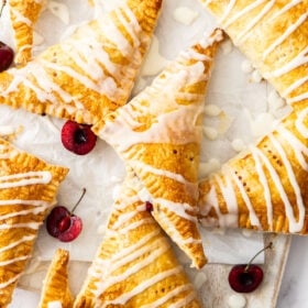 cherry puff pastry turnovers topped with a homemade glaze on a marbled board with sliced cherries.