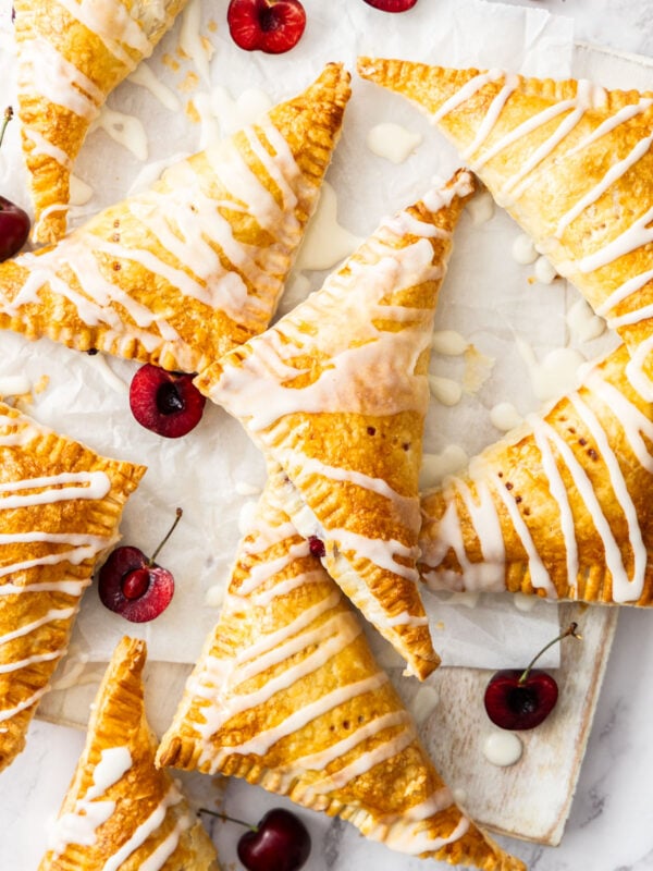 cherry puff pastry turnovers topped with a homemade glaze on a marbled board with sliced cherries.