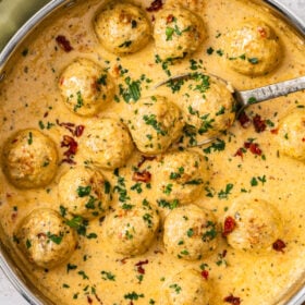 a skillet of marry me chicken meatballs in a creamy pan sauce topped with chopped parsley and sundried tomatoes.