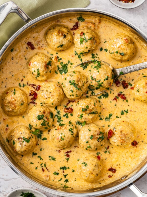 a skillet of marry me chicken meatballs in a creamy pan sauce topped with chopped parsley and sundried tomatoes.