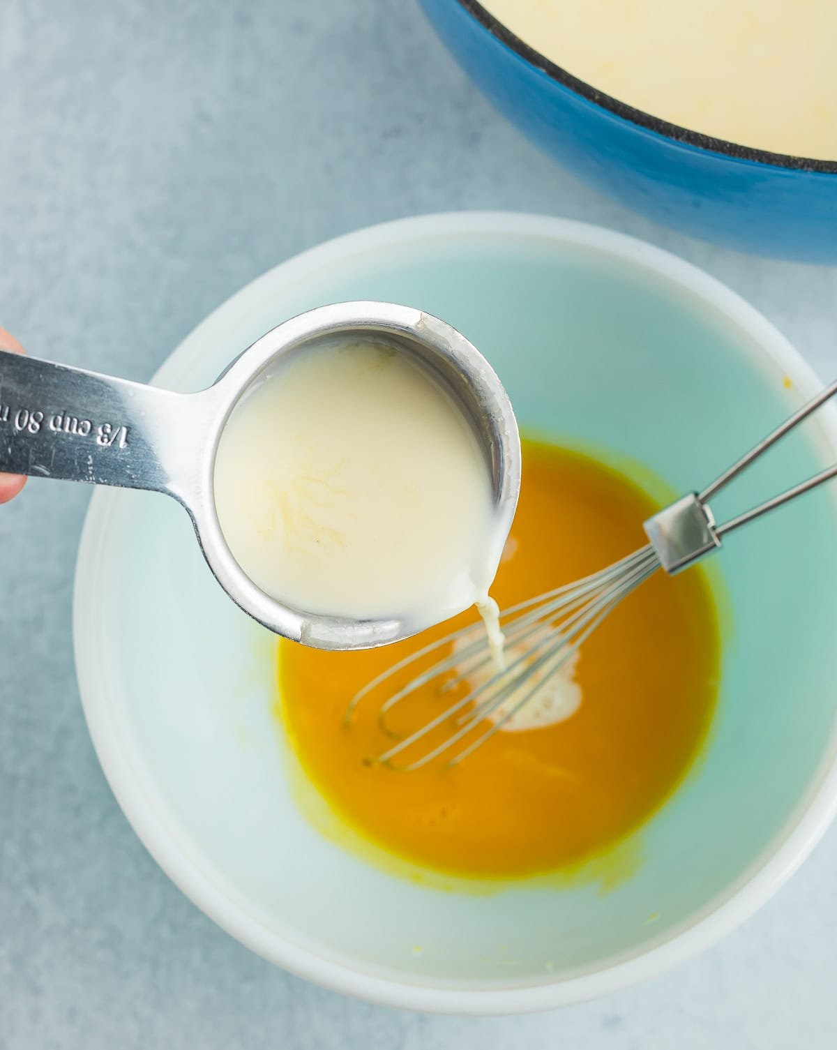 a measuring cup pouring milk into a bowl of whisked eggs.