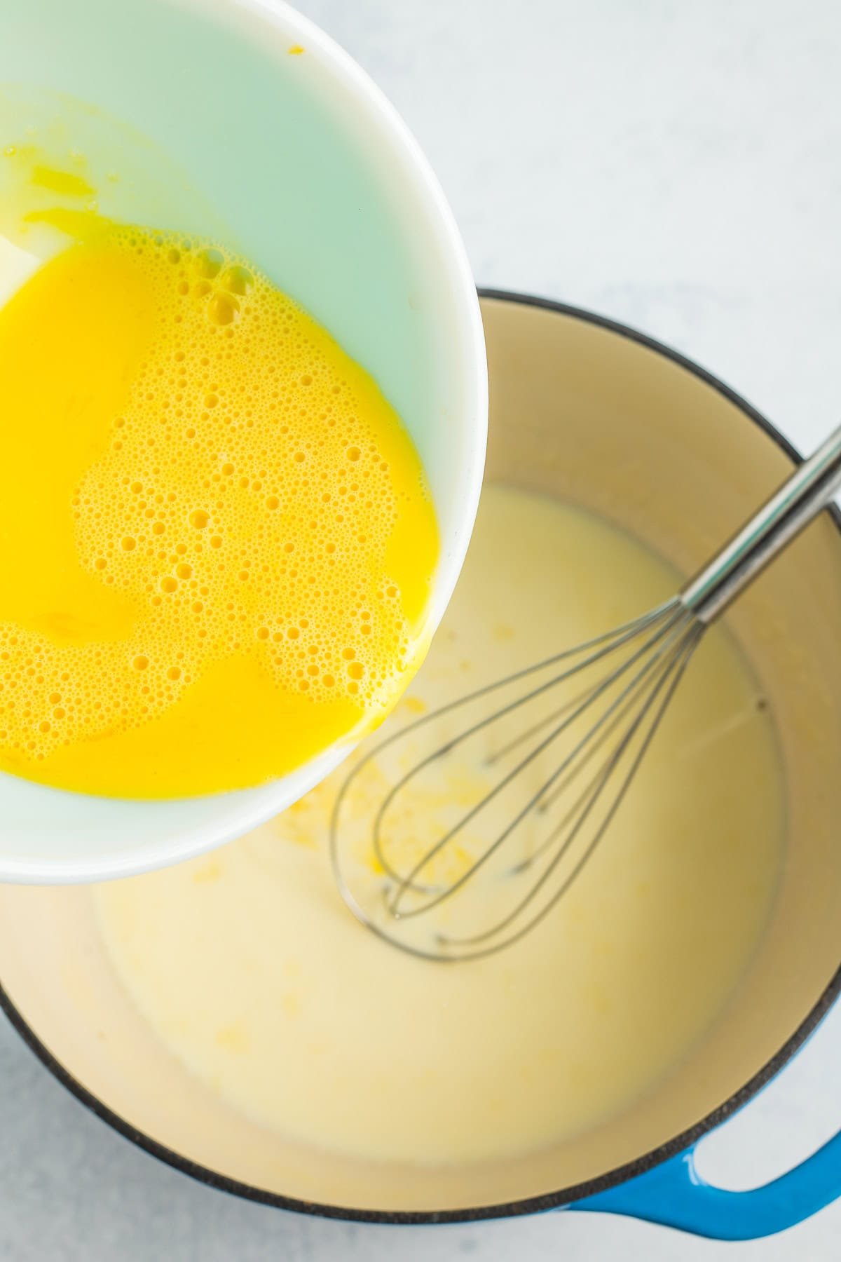 a bowl of eggs being poured into a blue Dutch oven.