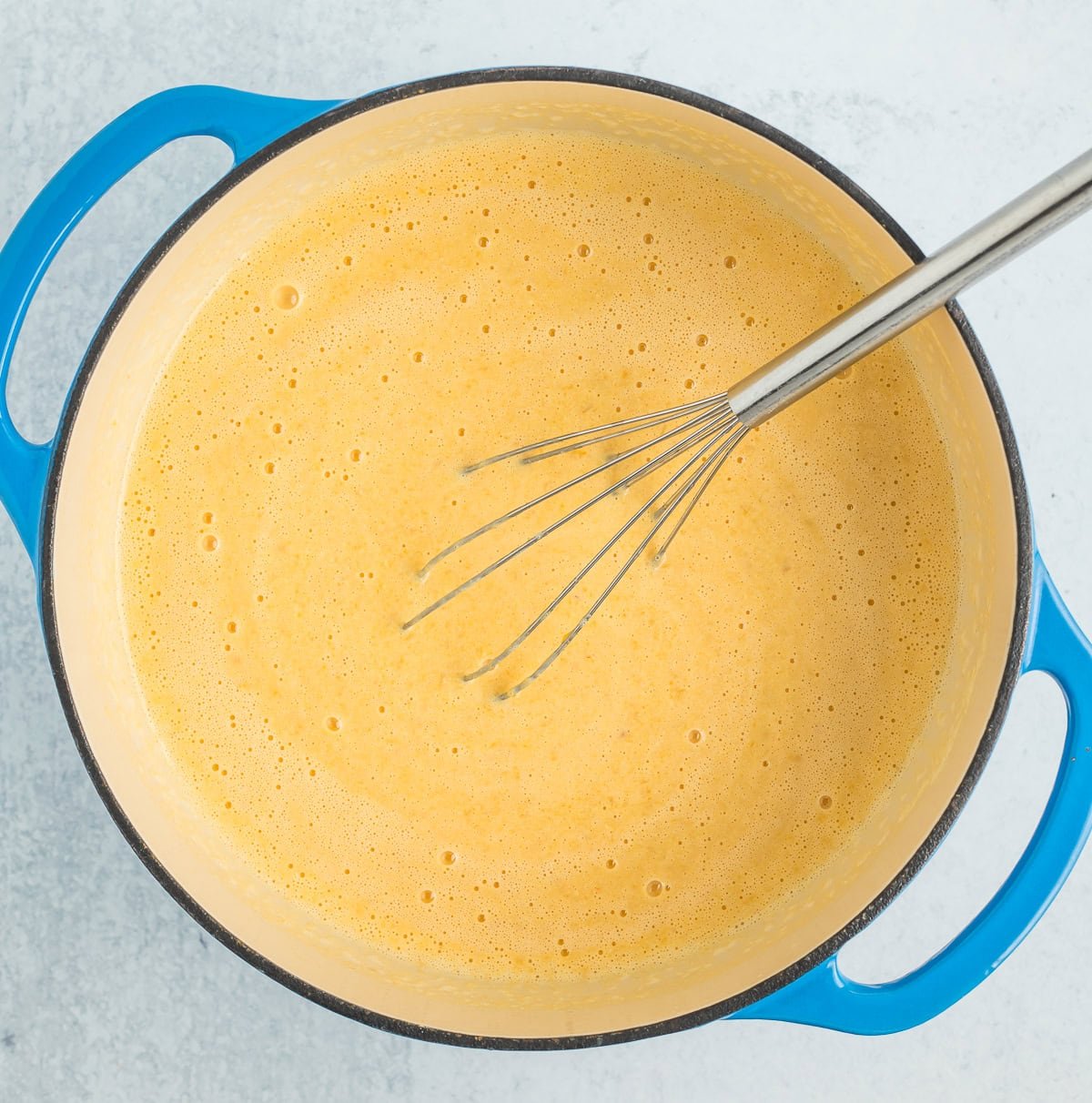 a blue dutch oven full of an orange liquid with a whisk.