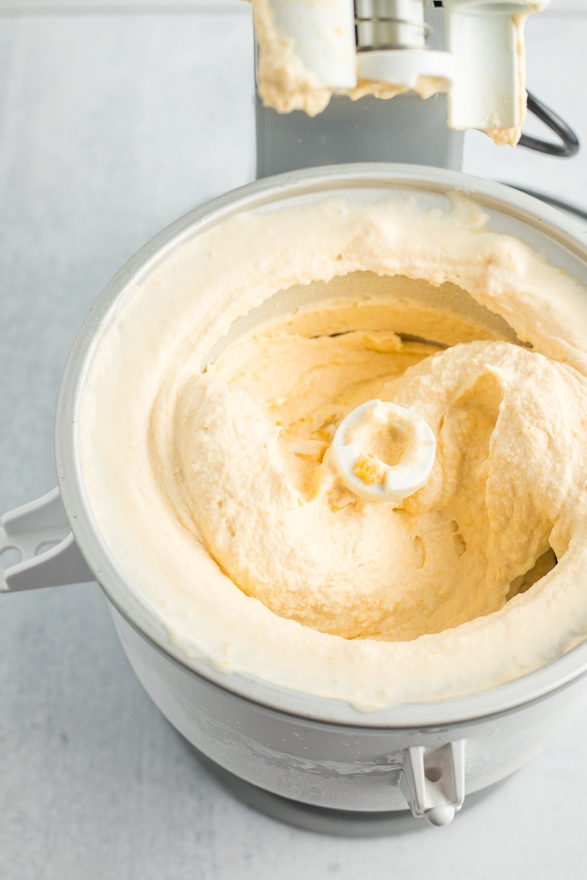 a kitchen aid mixer with an ice cream bowl showing churned homemade peach ice cream.