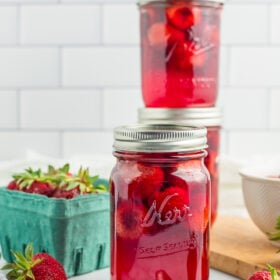 3 jars of strawberries on a marbled board with fresh strawberries in a small cardboard pint.
