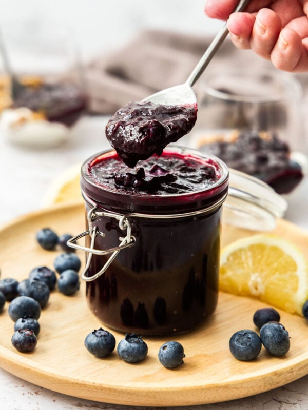 a hand holding a spoonful of blueberry compote over a glass jar.