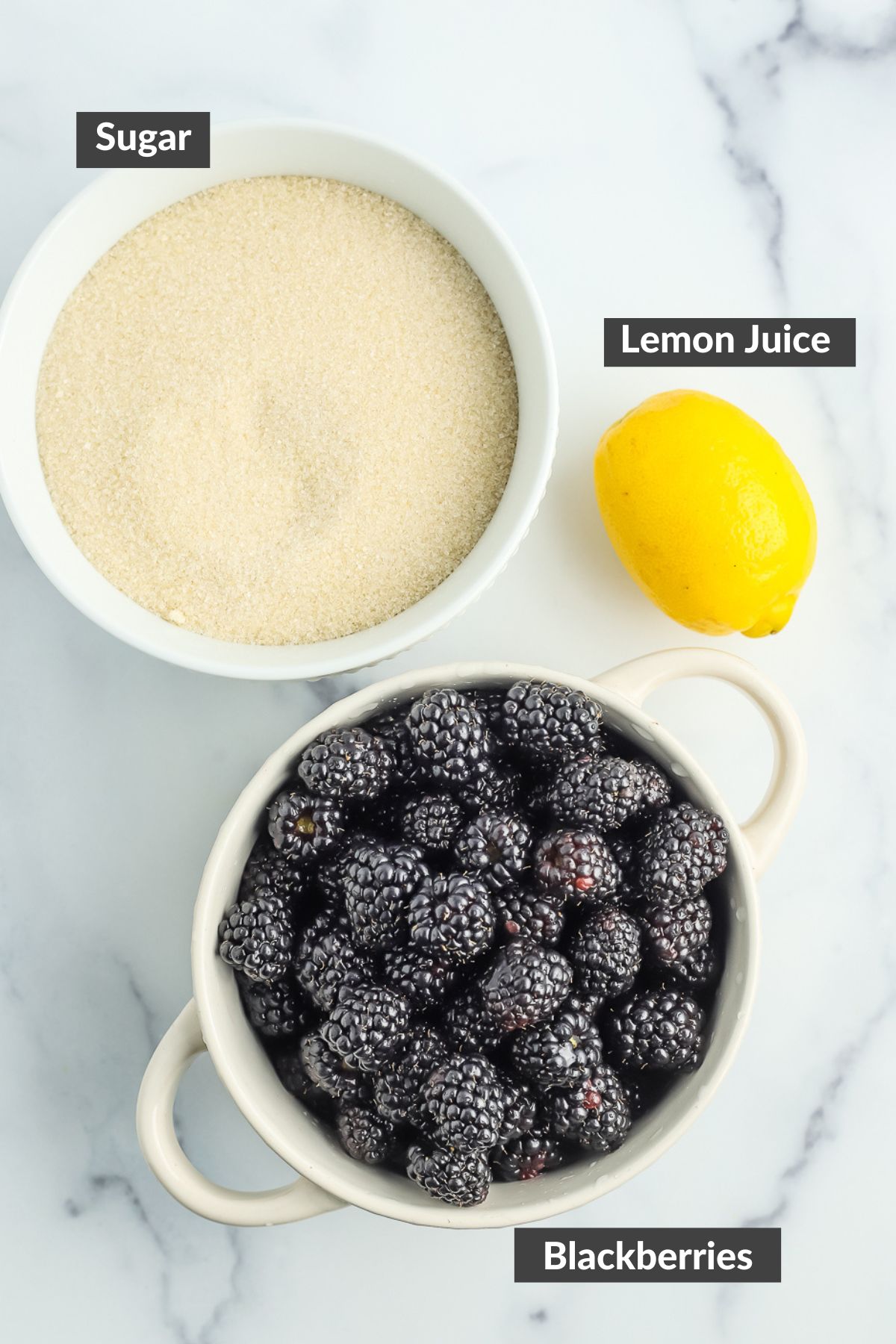 a bowl of blackberries, a bowl of sugar, and a lemon on a marble board.