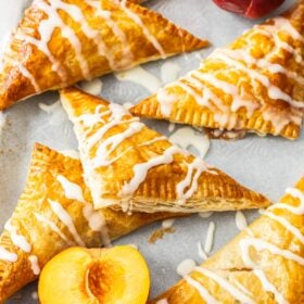 peach puff pastry turnovers on a baking sheet with sliced and whole peaches.