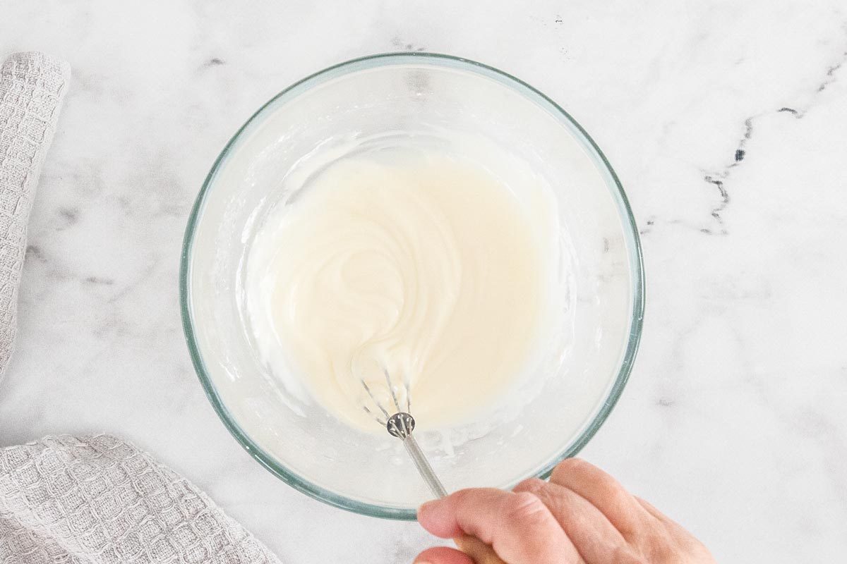 a glass bowl with an icing being whisked.