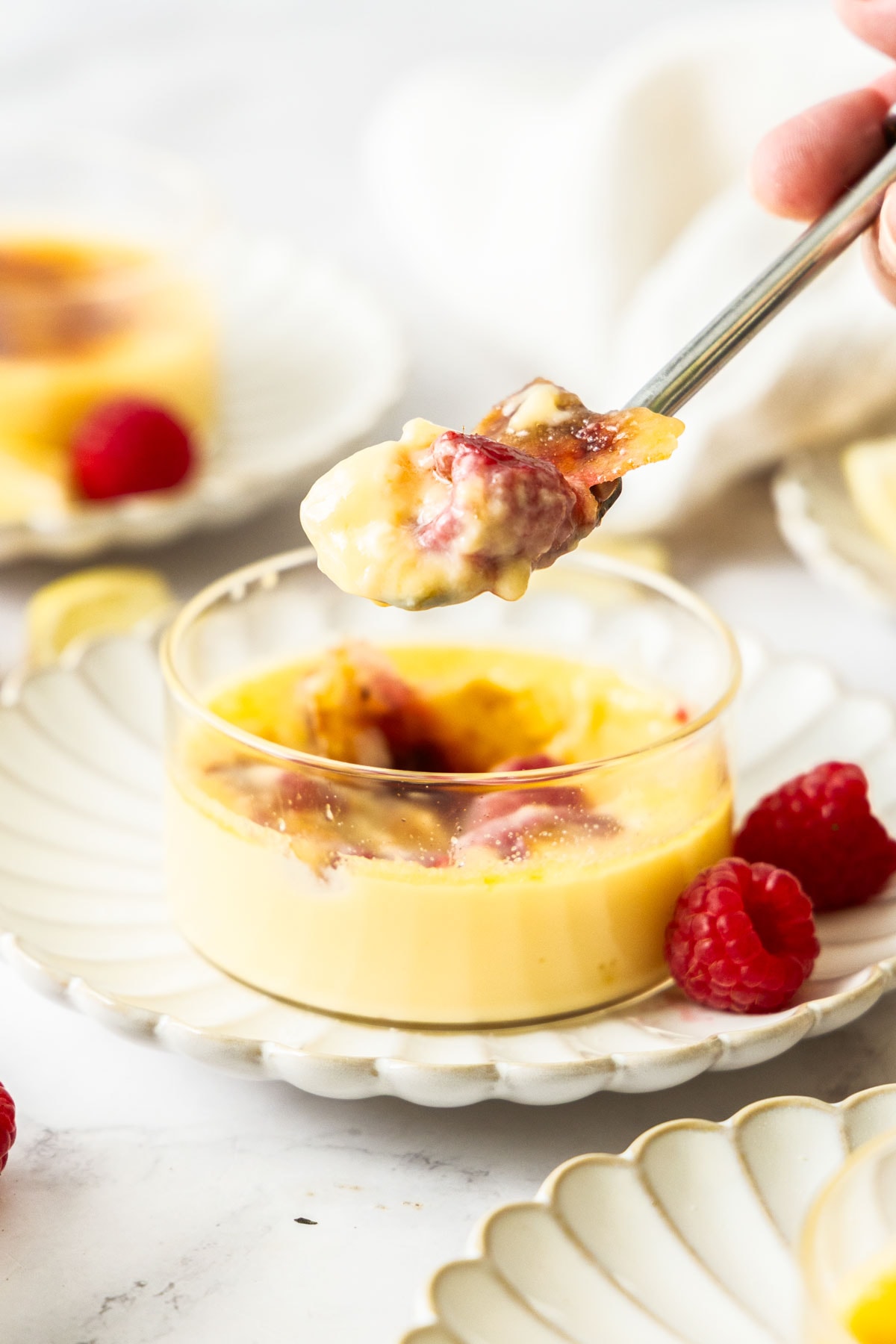 a spoonful of raspberry lemon creme brulee being scooped from a glass bowl.