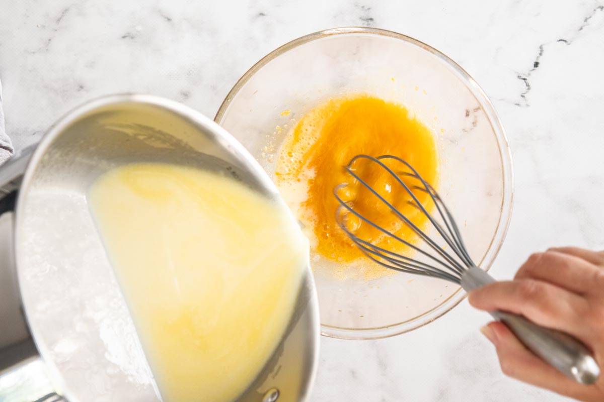 a saucepan of milk tempering a glass bowl of egg yolks.