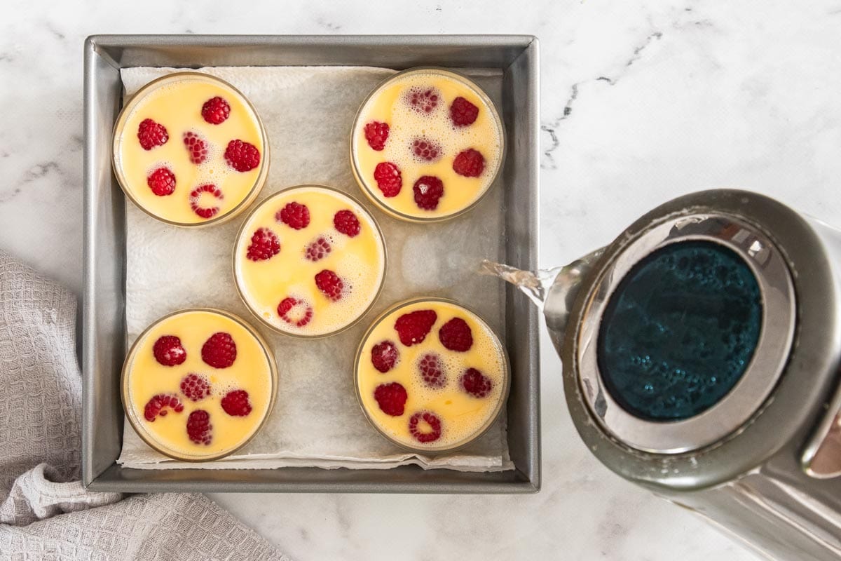 a kettle pouring water into a tray of custards.