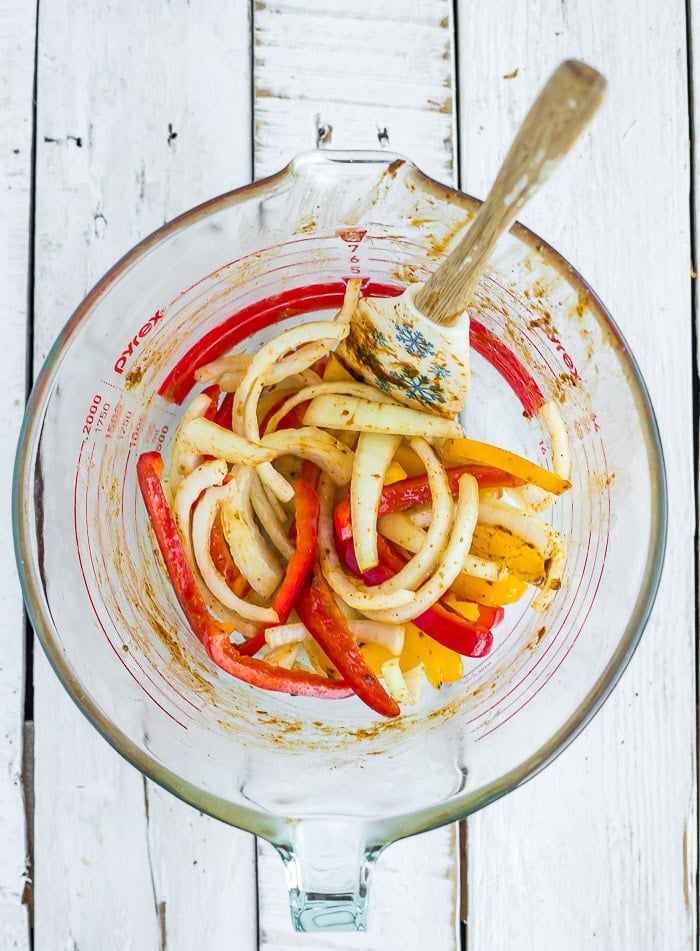 onions and peppers sliced in a glass bowl with a spatula.