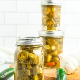 jars of canned pickled jalapeños with fresh jalapeños and garlic.
