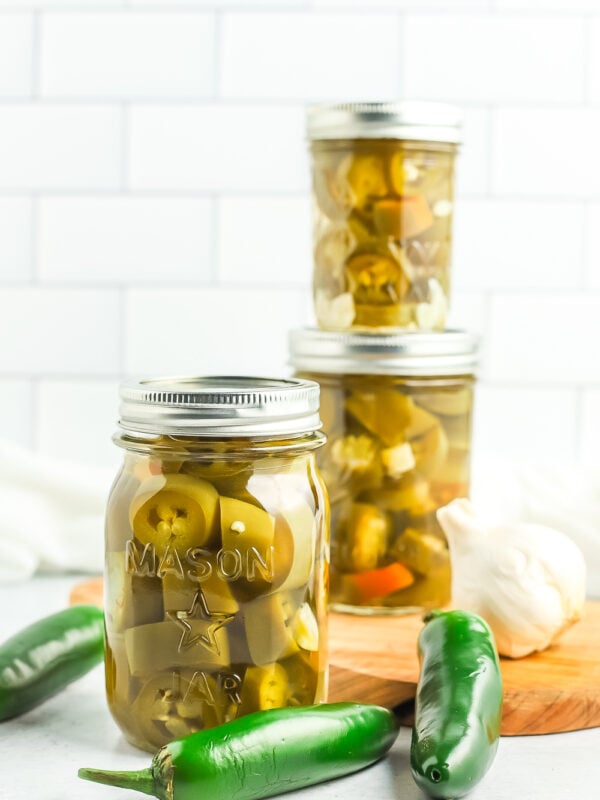 jars of canned pickled jalapeños with fresh jalapeños and garlic.