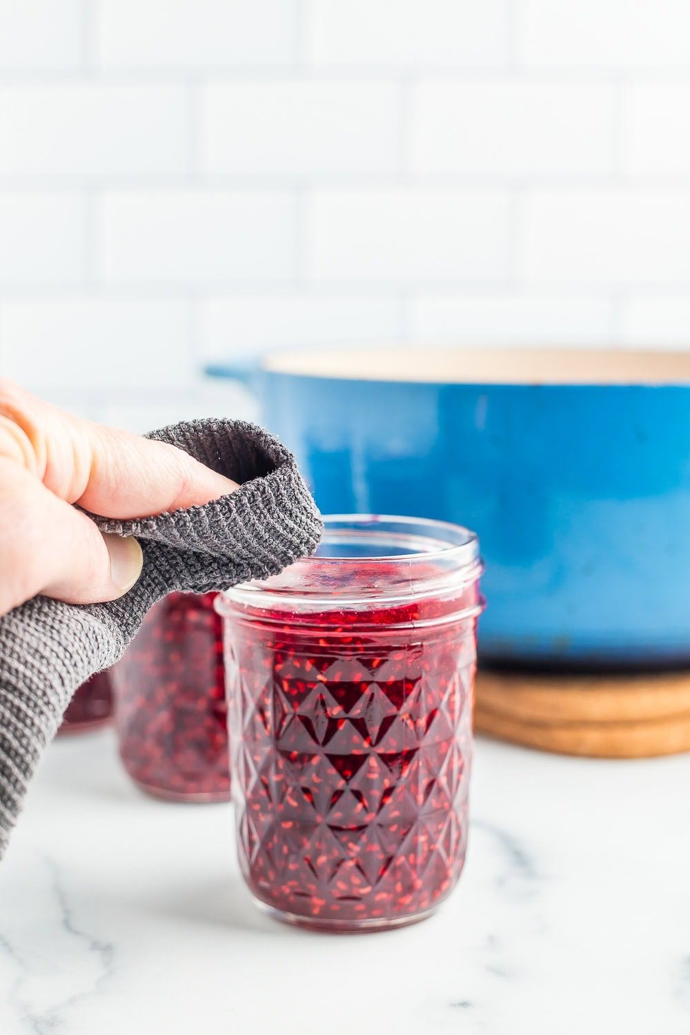 a grey cloth wiping the rim of a canning jar.