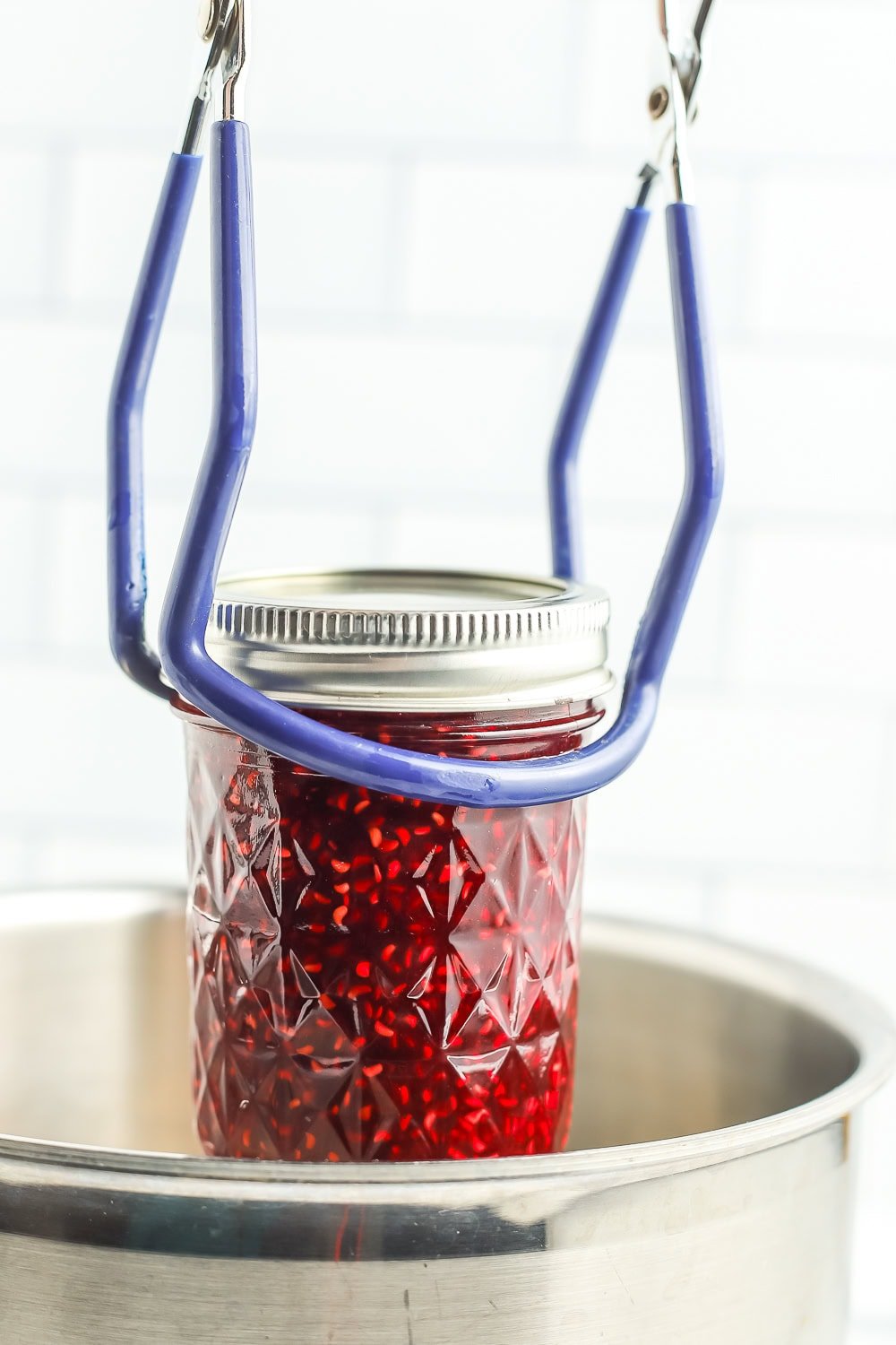 canning tongs holding a canning jar over a pot.