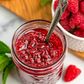 an open jar of raspberry jam with a spoon in it.