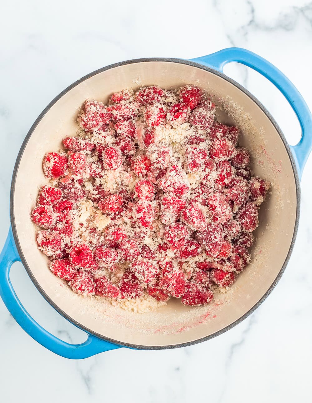raspberries coated with sugar in a blue Dutch oven.