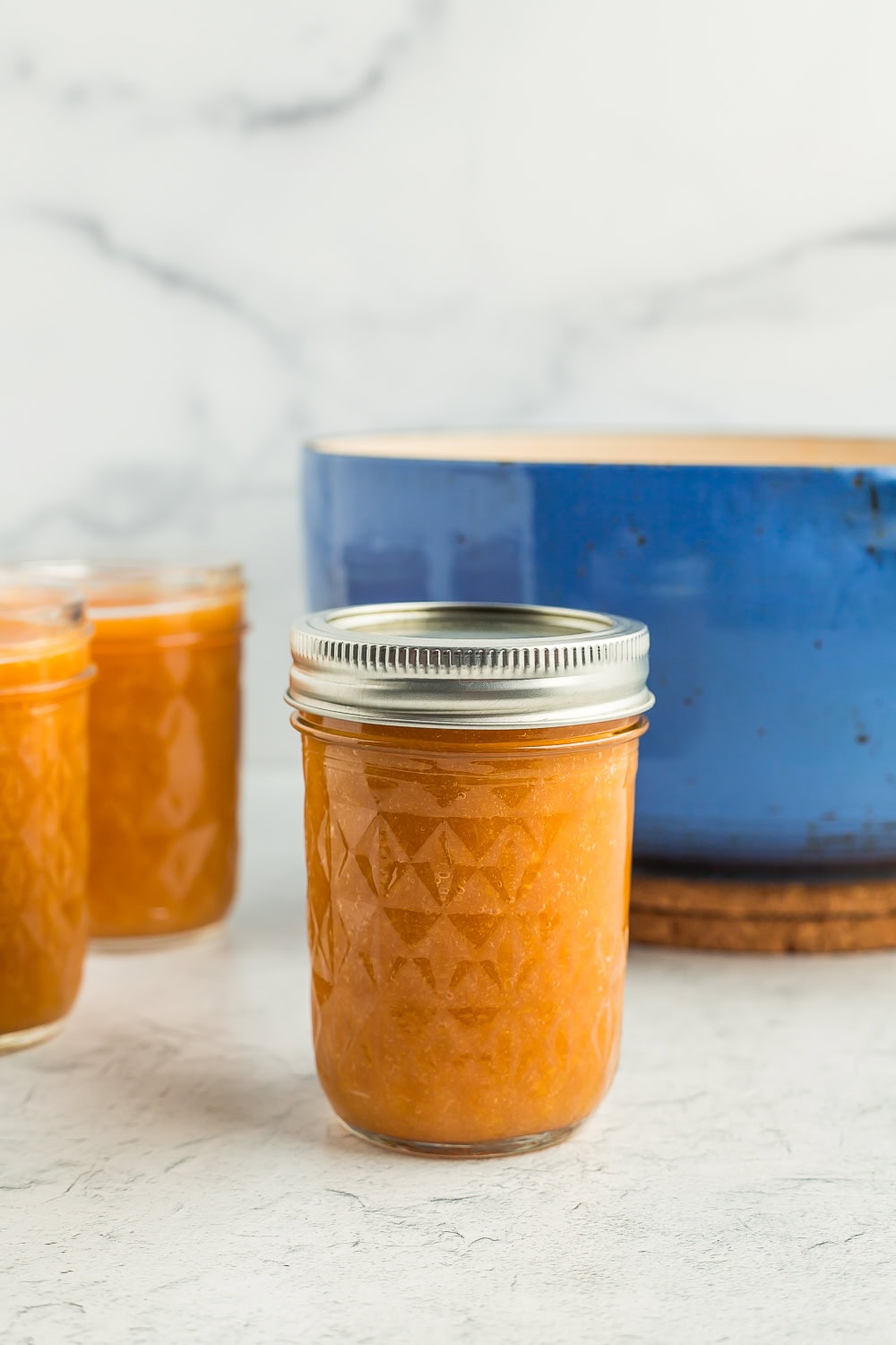 a canning jar of jam in front of a blue Dutch oven.