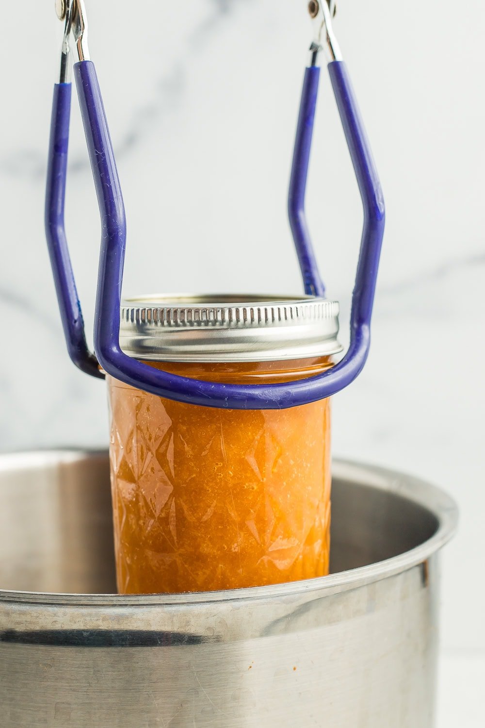 canning tongs lifting a jar into a canner.
