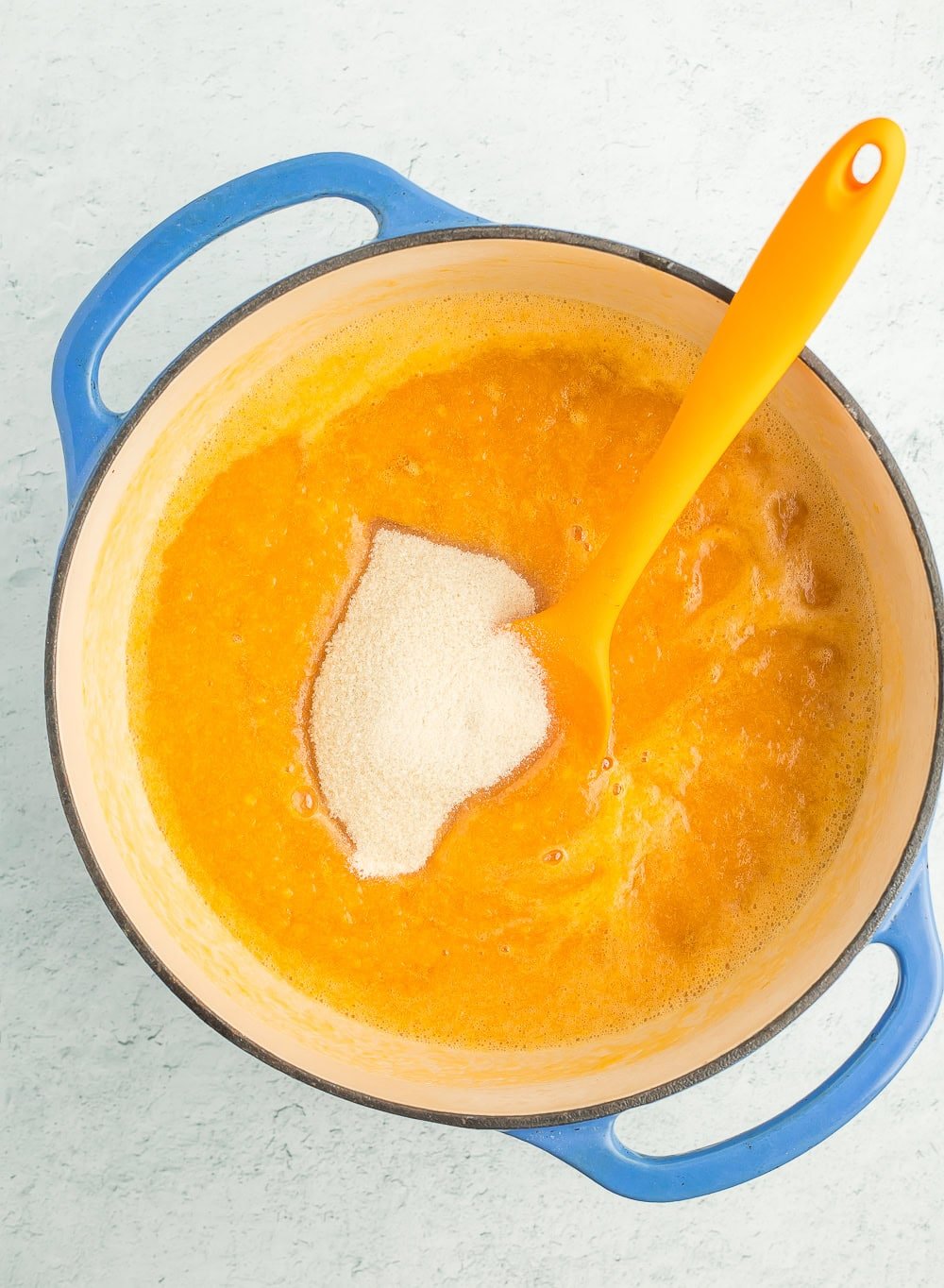 sugar and fruit puree in a blue Dutch oven with an orange spatula.