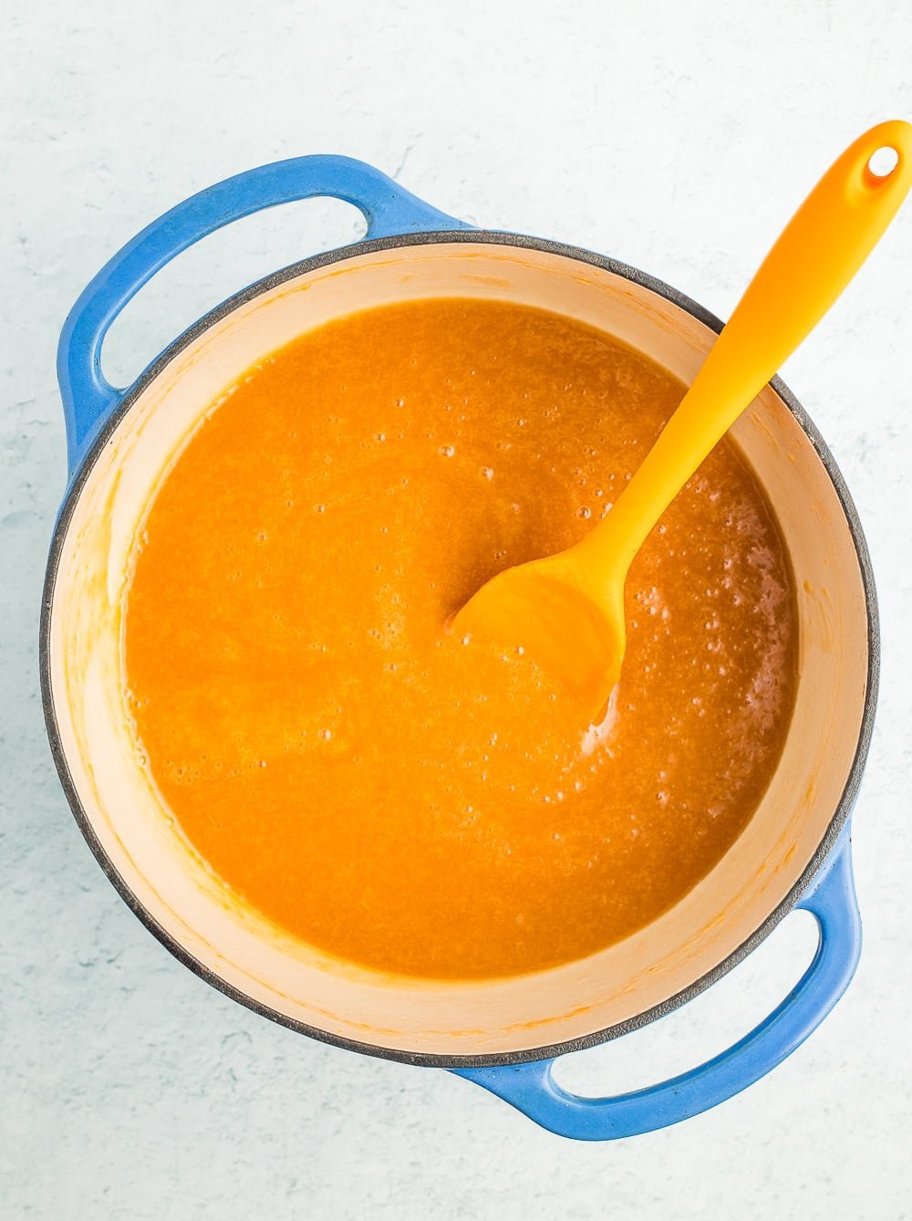 fruit spread in a blue Dutch oven with an orange spatula.
